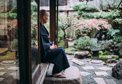 Side view of man looking away while sitting by house