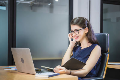 Young woman using phone while sitting on table