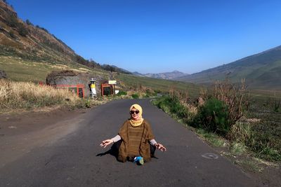 Full length of woman sitting on road against clear sky