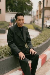 Portrait of young man sitting on footpath