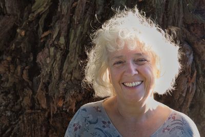 Portrait of a beautiful gray-haired seventy-year-old woman. against the background of a tree trunk. 