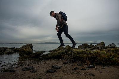 Hiker walks across mossy muddy stones from structure on bayside beach