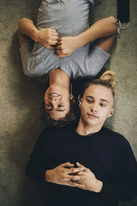 Smiling male teenagers listening music while lying on carpet at home