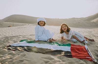 Portrait of happy siblings with united arab emirates flag at desert