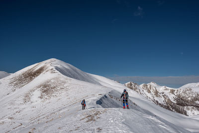 People on snowcapped mountain against clear sky
