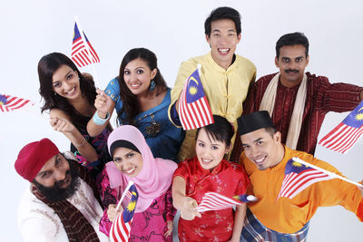 Portrait of people wearing traditional clothing holding malaysian flags against white background