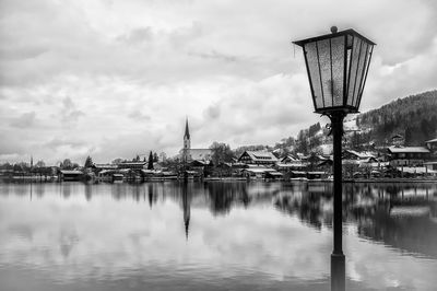 Reflection of street light on river by buildings against sky