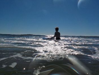 Man sitting on beach against clear sky