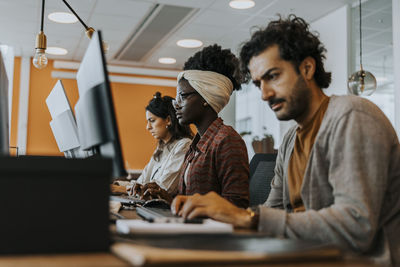 Multiracial colleagues using computer while working at desk in corporate office