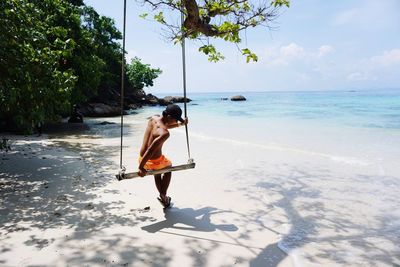 Rear view of man sitting on beach swing against sky