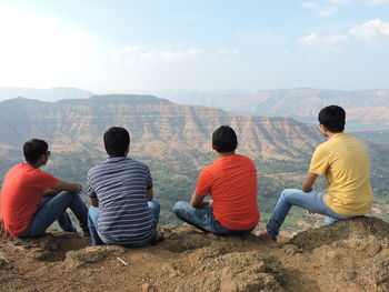 Rear view of people sitting on mountain against sky
