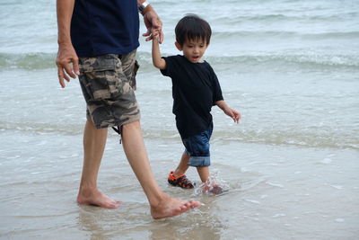 Son holding hands of father while walking in water at beach