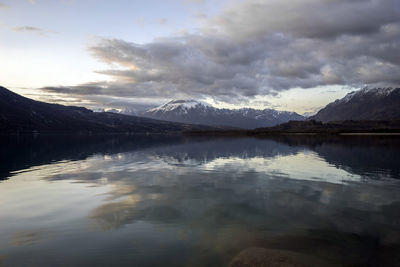 Scenic view of lake with mountains and clouds reflection at sunset