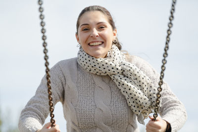 Portrait of smiling young woman swinging against clear sky