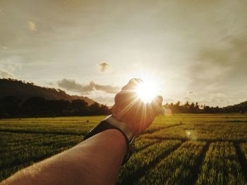 Optical illusion of cropped hand holding sun on field against sky