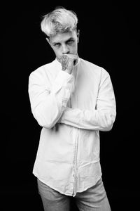 Portrait of young man standing against black background