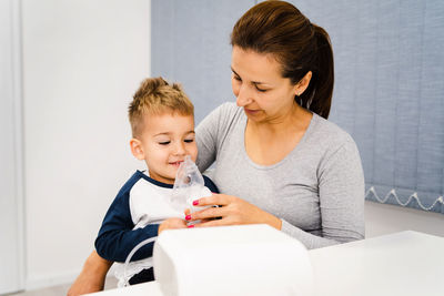 Smiling mother sitting with son wearing oxygen mask