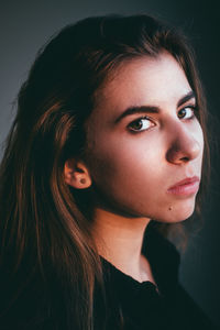 Close-up portrait of young woman against gray background