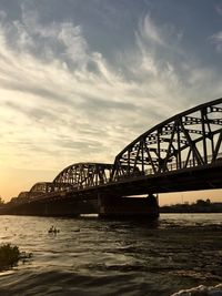 Silhouette of bridge over river against cloudy sky