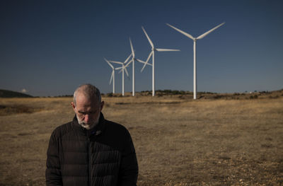 Adult man in winter cloth with modern windmills against blue sky. shot in castilla la mancha, spain