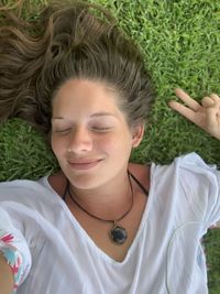 Portrait of  young women lying on grass with her eyes closed giving a peace sign 