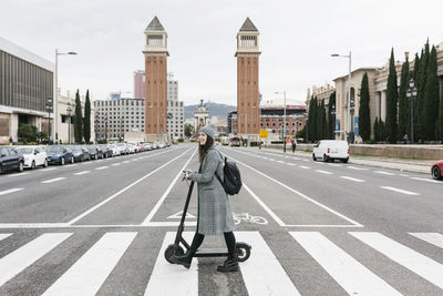 Woman with electric push scooter crossing road in city