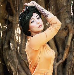 Beautiful fashion model posing against tree trunk