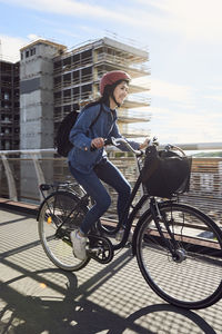 Smiling mid adult woman cycling on footbridge against sky