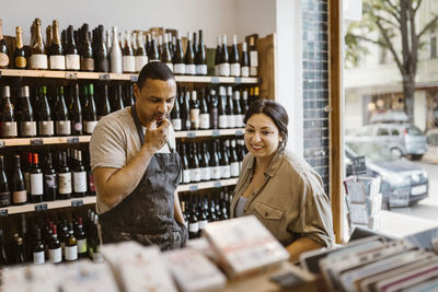 Male owner with hand on chin standing with female colleague at wine shop