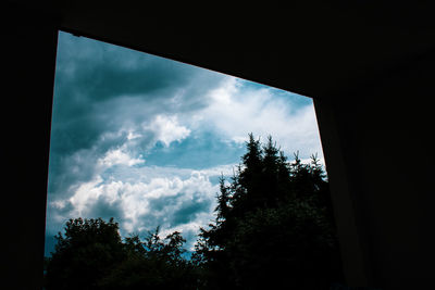 Low angle view of silhouette trees against sky seen through window