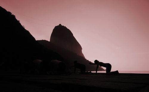 Silhouette man on rock against clear sky during sunset