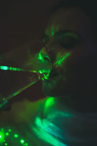 Close-up of young woman drinking wine against illuminated background