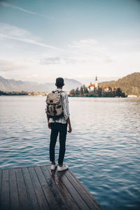 Rear view of man standing on pier over lake against sky