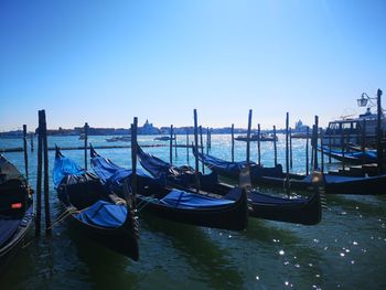 Gondolas moored in canal against clear blue sky