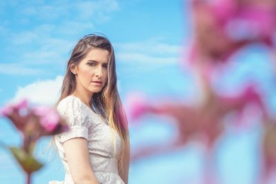 Portrait of beautiful young woman standing against sky