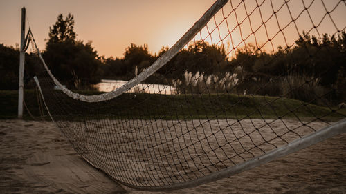 Close-up of hammock by fence against sunset