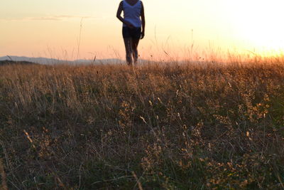 Low section of woman standing on field against sky during sunset