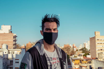 Portrait of young man with face mask in city against clear sky