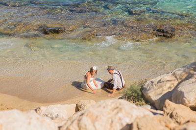 High angle view of friends relaxing on rock at beach