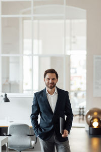 Male entrepreneur holding digital tablet while standing with hand in pocket at office