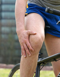 Midsection of man with bicycle touching knee in pain