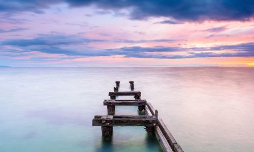 View of jetty on calm sea against cloudy sky