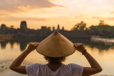 Rear view of woman wearing hat against sky during sunset