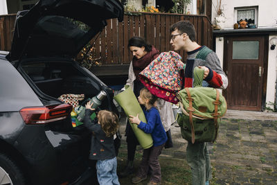 Excited family loading picnic stuffs in electric car trunk outside house
