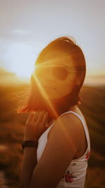 Portrait of woman wearing sunglasses while standing on land against sky during sunset