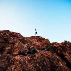 Man standing on rock by mountain against clear sky