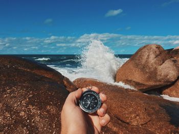 Cropped image of person holding navigational compass against rocky shore