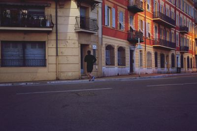 Rear view of man walking on road against buildings