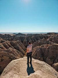 Rear view of man standing on rock against sky