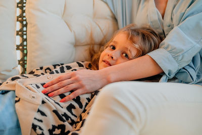 A small, happy girl, a child on her mother's lap with a smile on the sofa at home